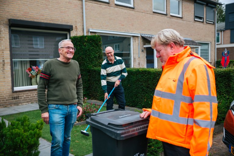 Drie mensen in gesprek bij afvalcontainer
