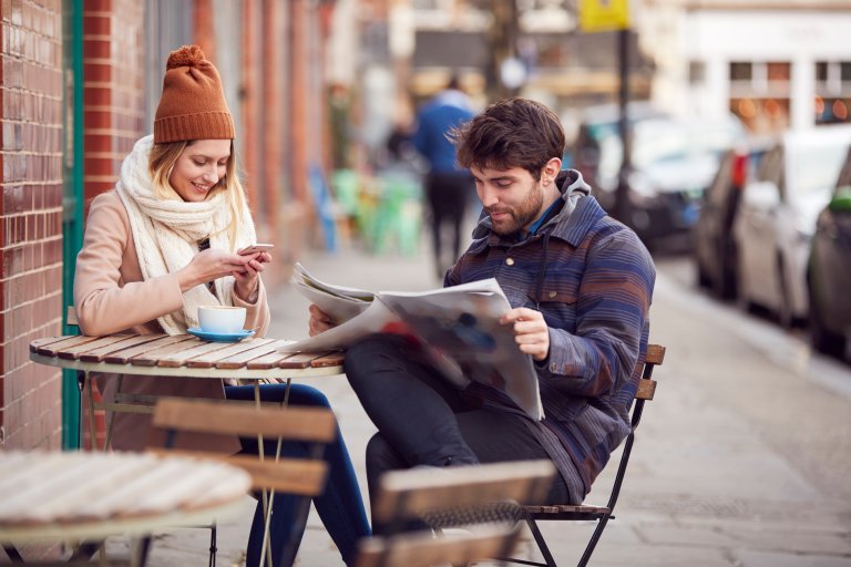 twee mensen op een terras waarvan de man de krant leest