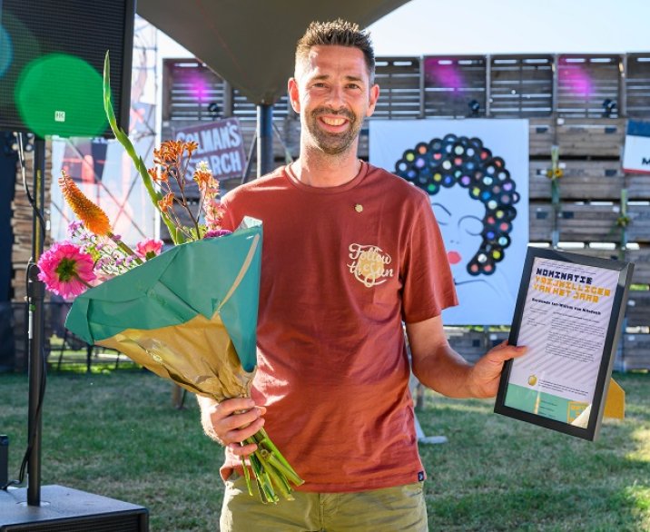 Jan-Willem met speldje Gouden Oogappel op zijn t-shirt gespeld, een bos bloemen in zijn rechterhand, de nominatie vrijwilligers van het jaar in zijn rechterhand